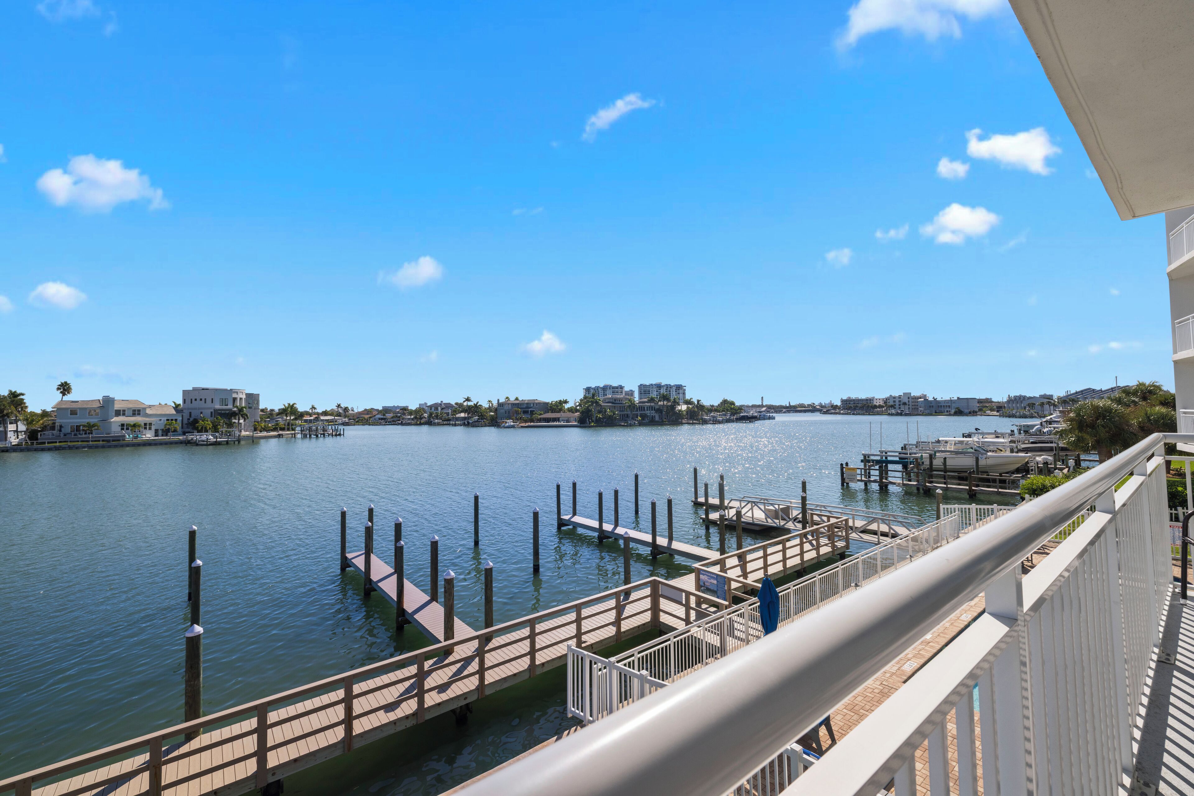 A waterfront view from a balcony with a dock, a clear sky, and buildings in the background.