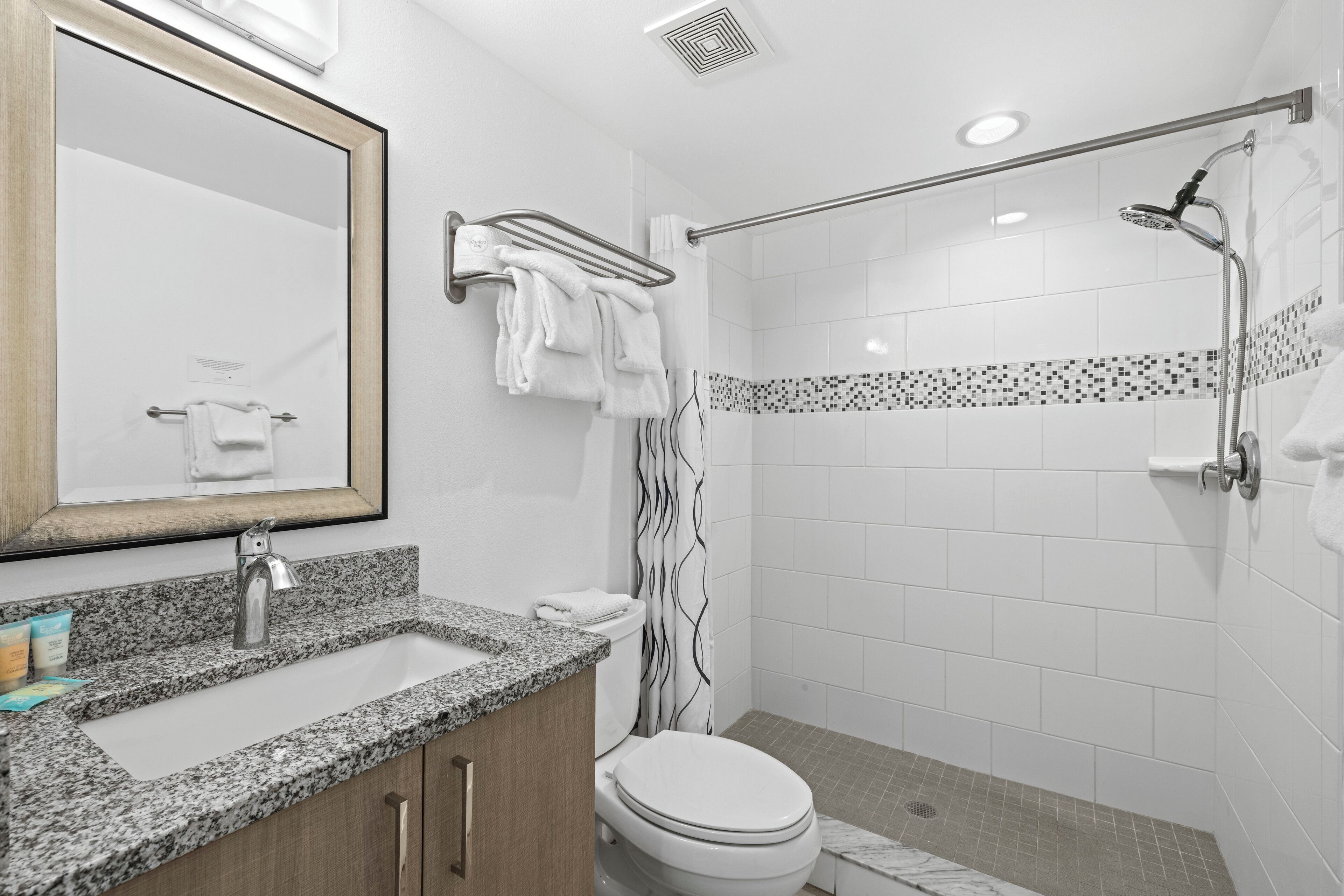 A modern bathroom with a granite countertop sink, a toilet, and a shower area.