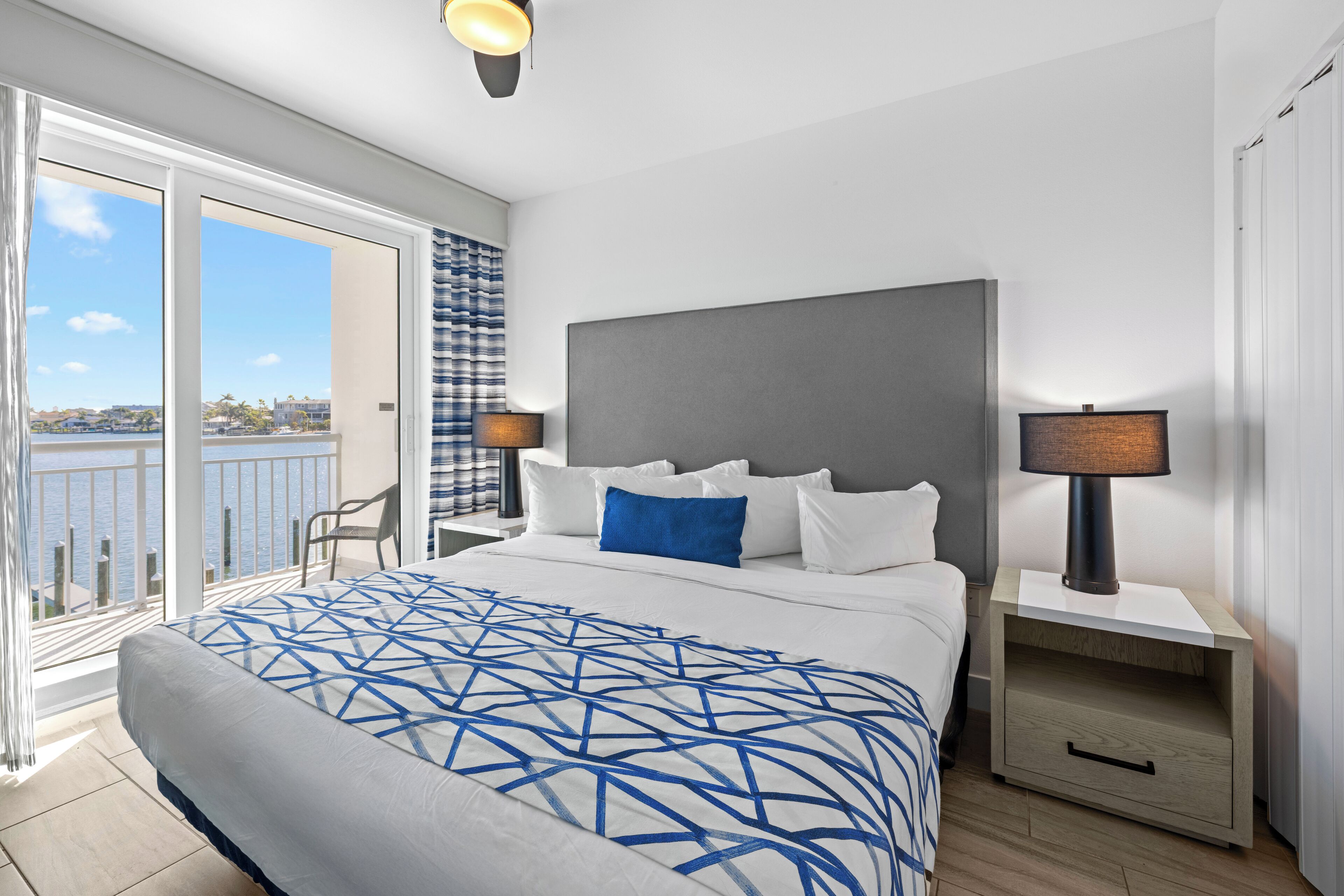 A bedroom with a large bed, two bedside tables, a chair, and a view of the outdoors.