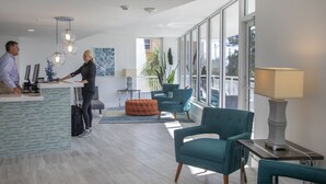 A modern hotel lobby with a reception desk, teal armchairs, a large window, and a minimalist decor.