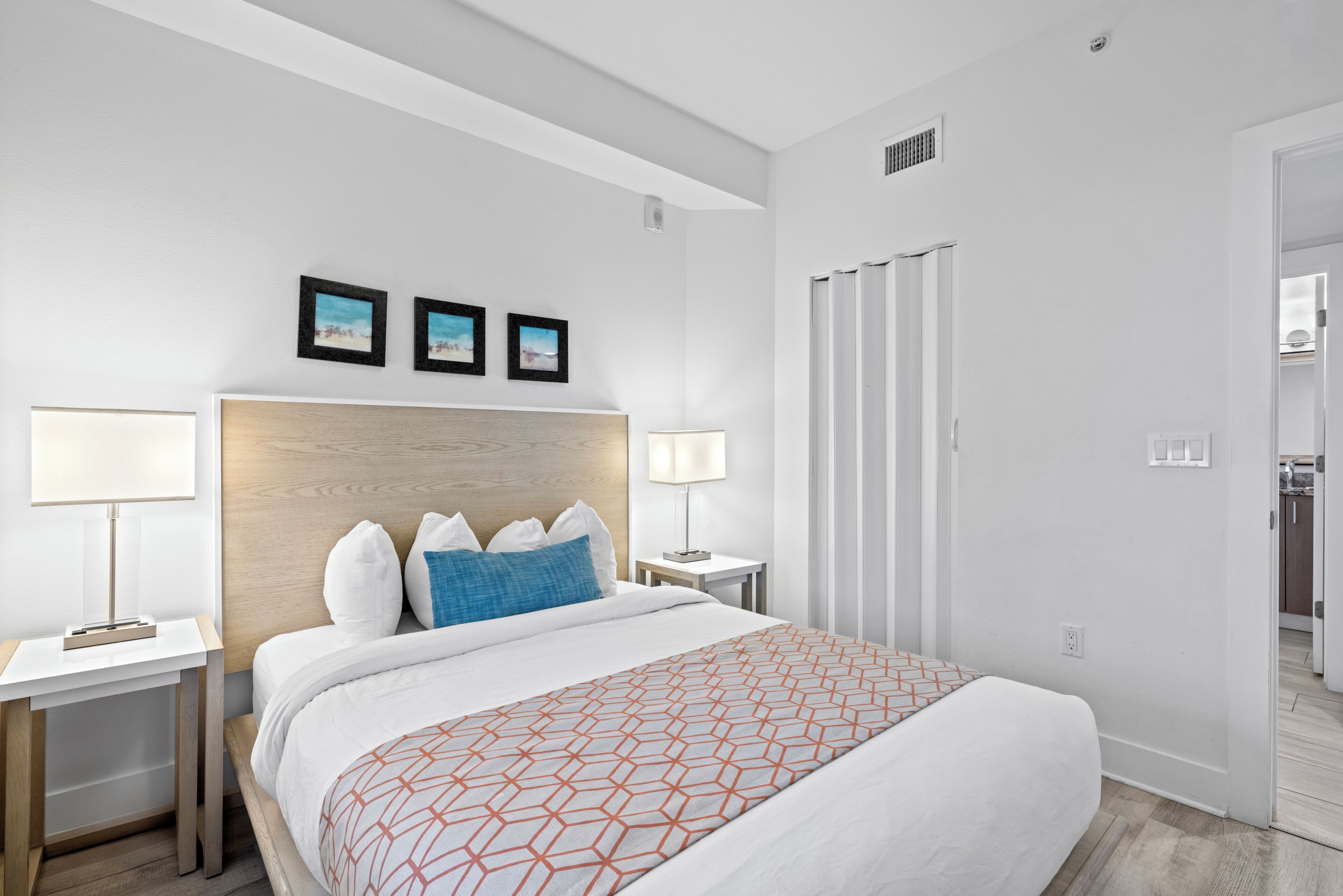 Habitación de hotel con una cama grande, dos mesitas de noche, un cabecero y tres cuadros enmarcados en la pared.