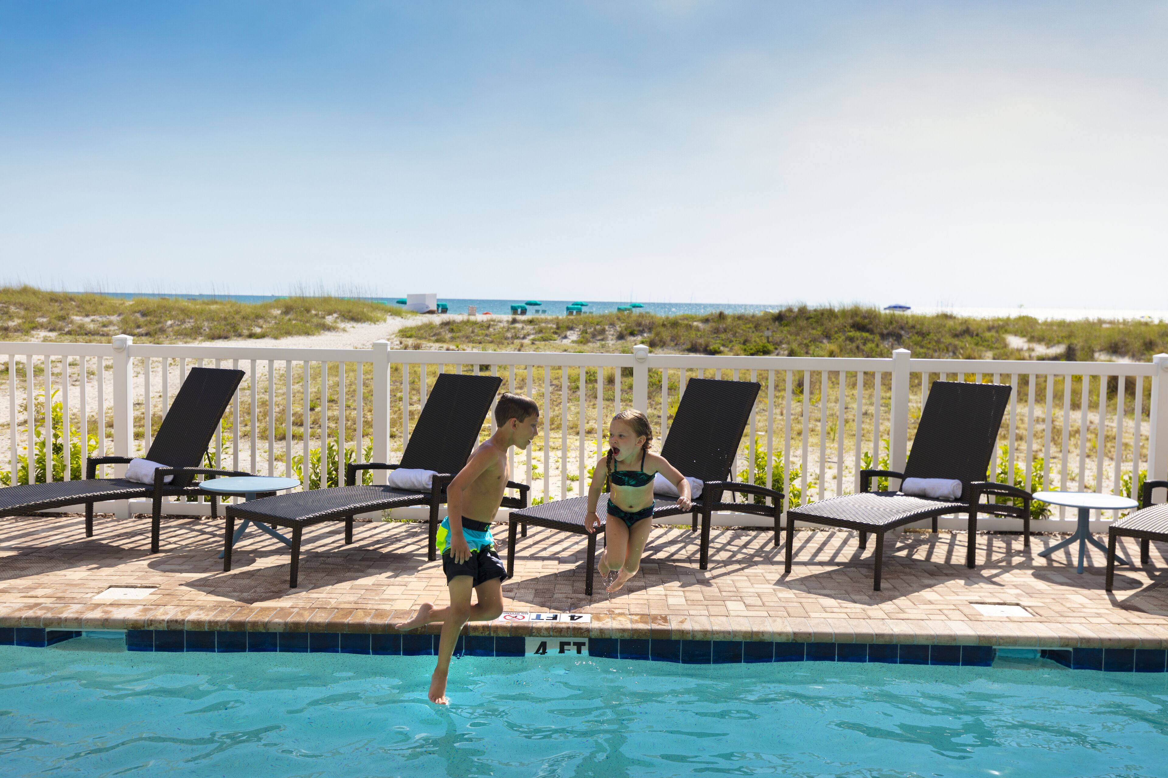 A pool area with lounge chairs and a view of the beach.