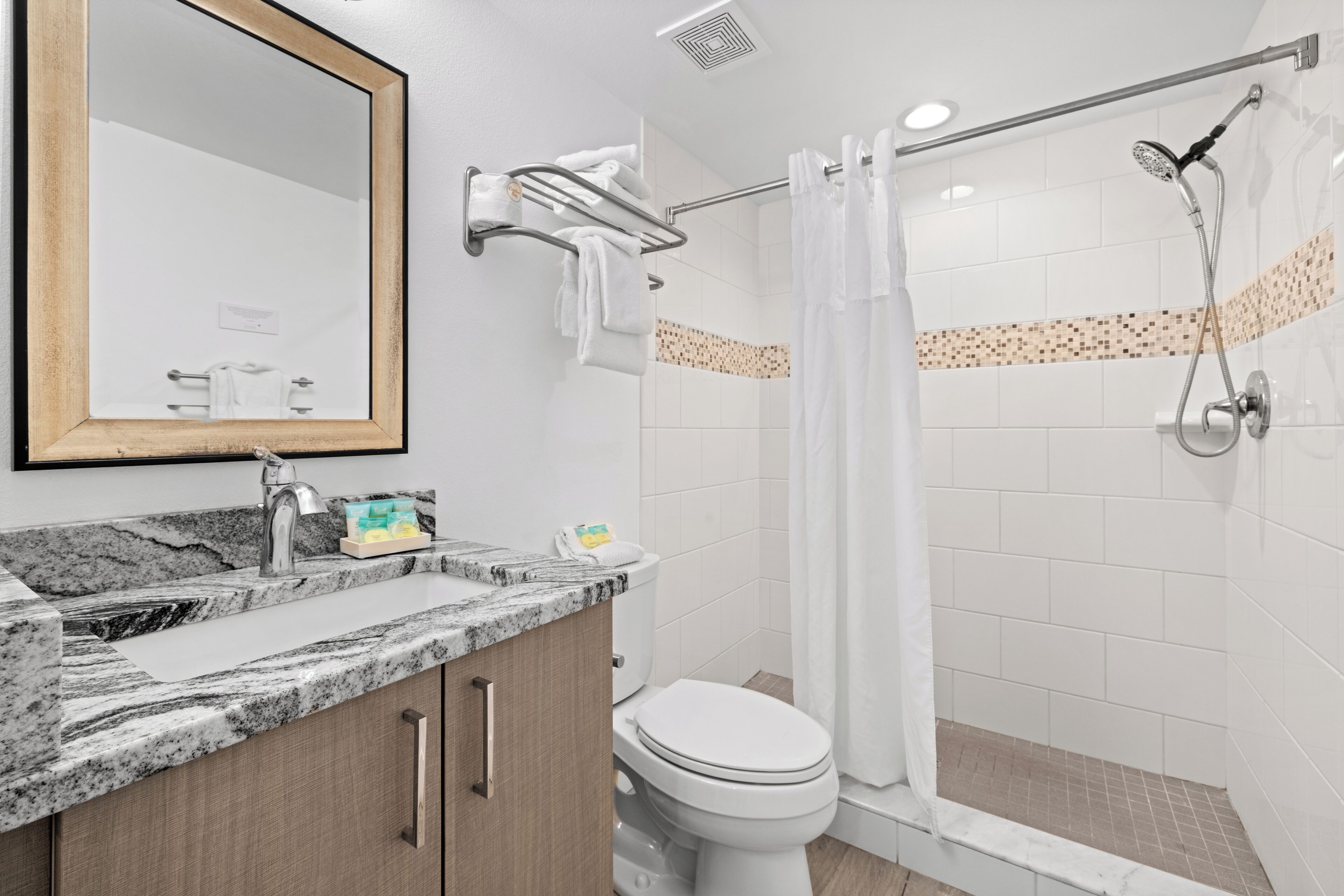 A bathroom with a marble sink, a toilet, a shower with a glass door, and a mirror with a wooden frame.