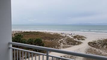 A beach view from a balcony with a railing, sandy beach, and ocean.