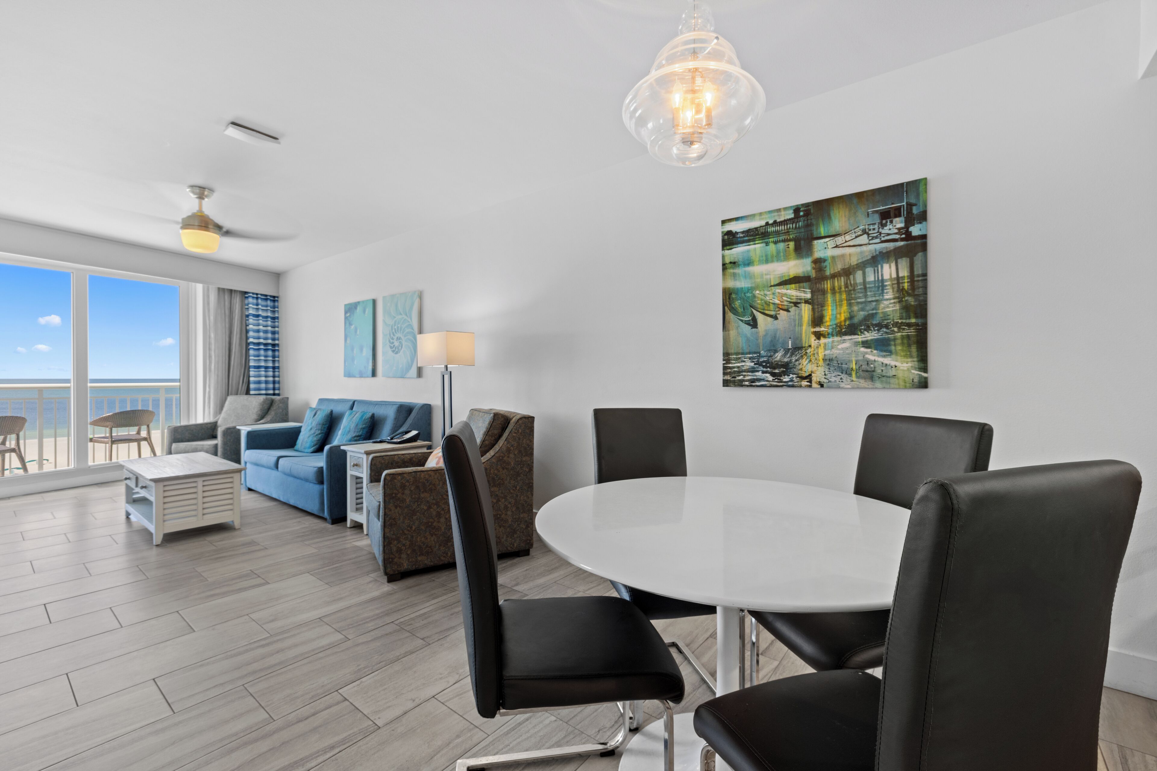 A modern living room with a white round table, black chairs, a blue sofa, and a painting on the wall.