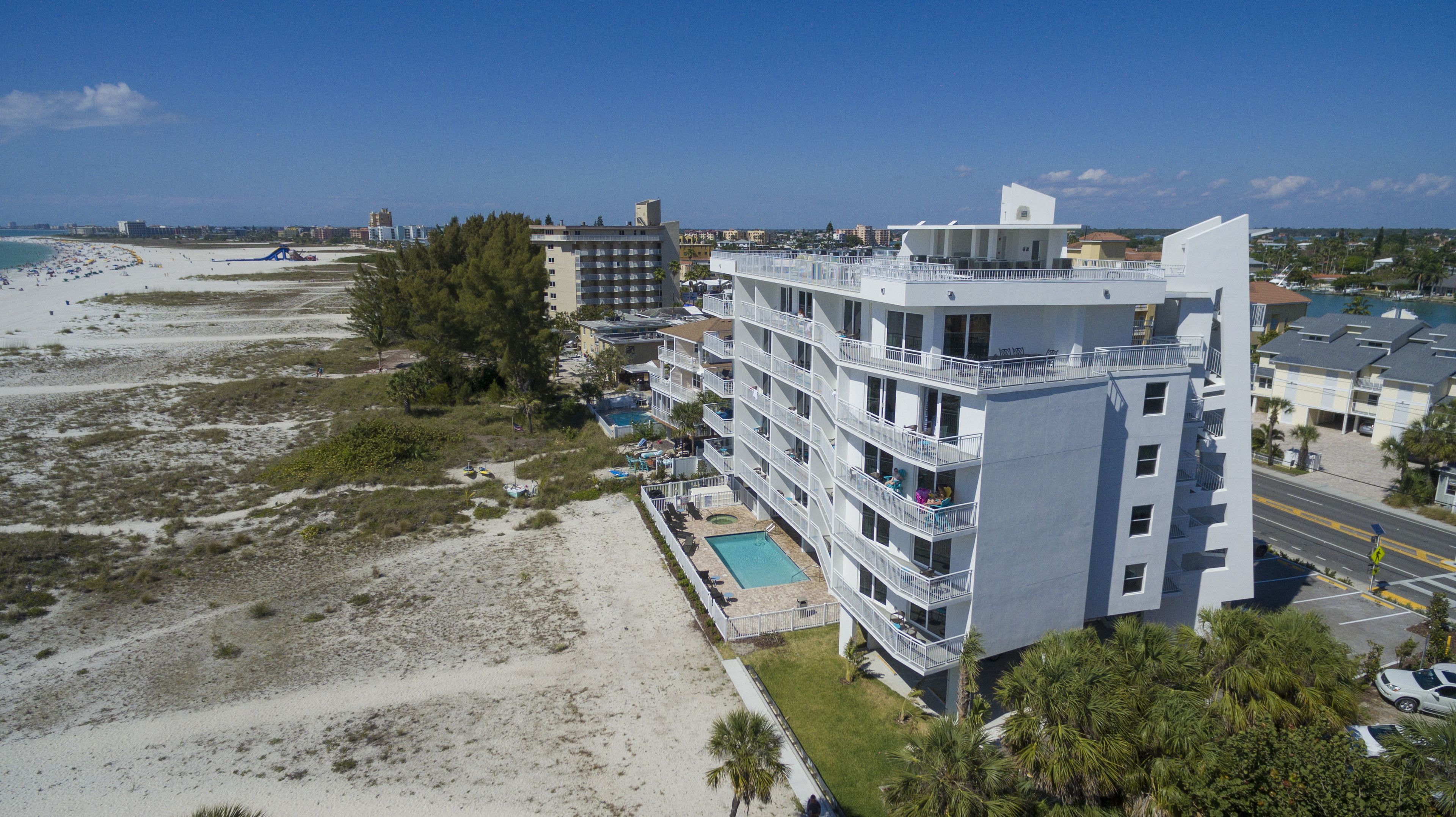 A multi-story hotel with balconies, a swimming pool, and a beach view.