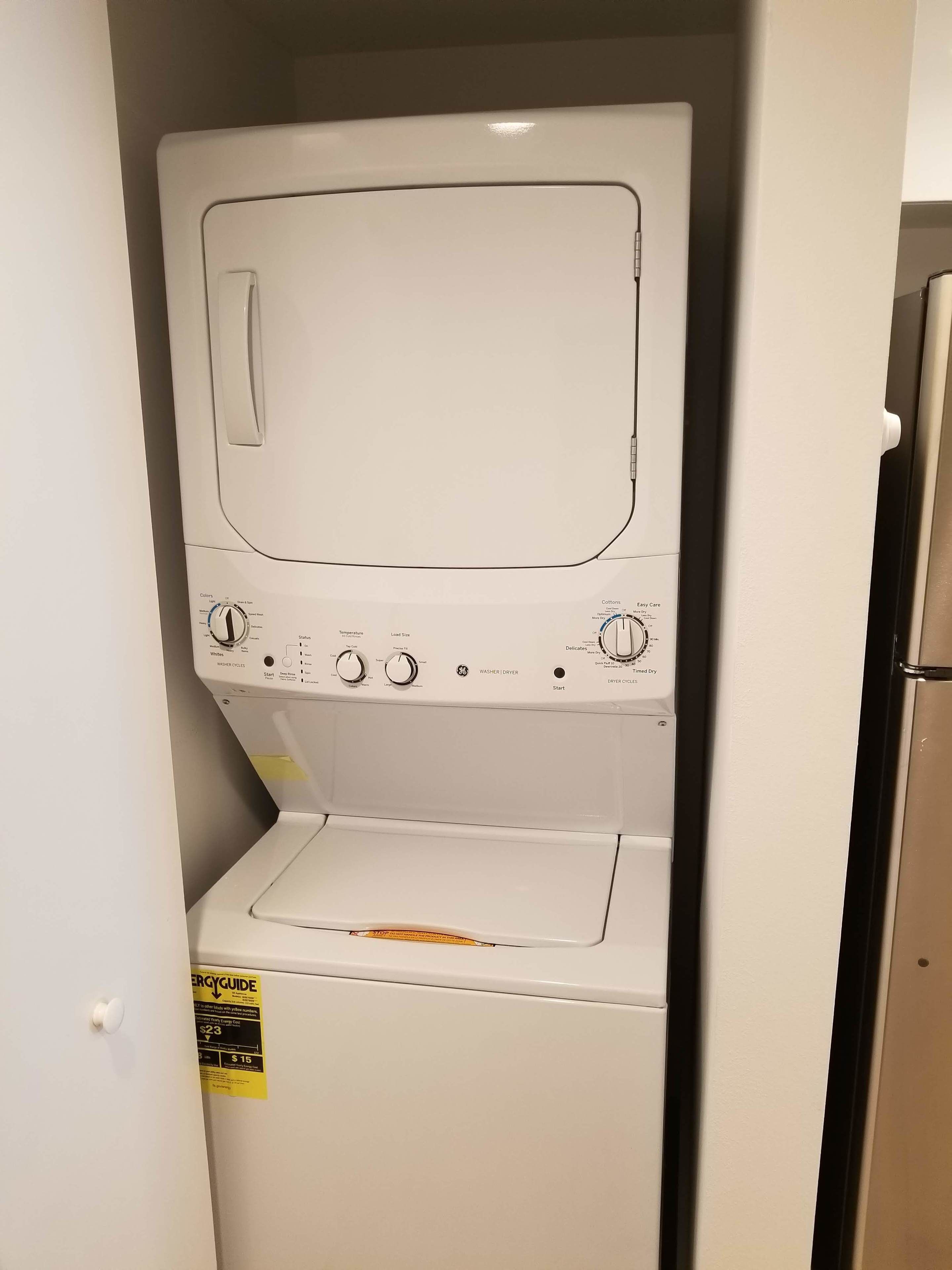 Una unidad compacta de lavadora y secadora con un panel de control que incluye perillas para seleccionar la temperatura y el ciclo, un botón de inicio y una etiqueta amarilla de EnergyGuide.