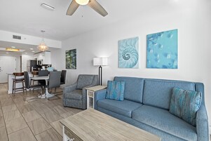 A modern living room with a blue sofa, a wooden coffee table, and a dining area with chairs and a table.