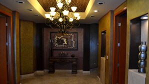 A hallway with a chandelier, a decorative wall piece, and a wooden bench.