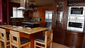 A kitchen with a central island, bar stools, a stainless steel refrigerator, and a built-in oven.