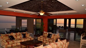 A spacious living room with a large window offering a view of the ocean, a ceiling fan, and a fireplace.