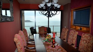 A conference room with a long table, patterned chairs, a chandelier, and a view of the sea.