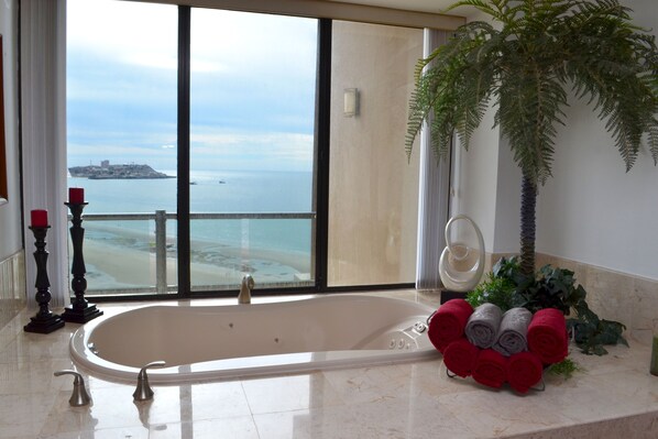 Un baño moderno con una bañera grande, vistas al océano y una planta en la encimera.