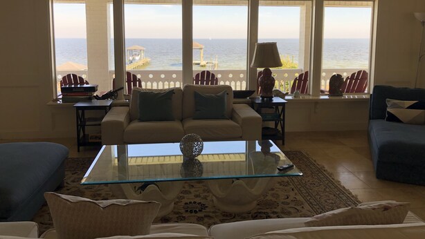Un salón con una mesa de centro de vidrio, dos sofás y vista al mar a través de amplios ventanales.