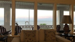 Un rincón acogedor con sofá y sillones, ventanas amplias con vista al mar y una lámpara sobre una mesa.