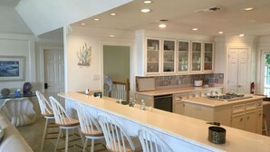 Una cocina con una isla central, taburetes de bar y una zona de comedor con sofá.
