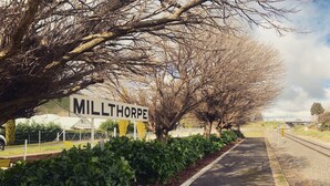 A road sign for 'MILLTHORPE' with a pathway lined by trees and shrubs.