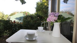 A white table with a white cup and saucer, a white vase with pink flowers, and a chair.