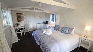 A bedroom with a large bed, a desk, a chair, a small table with a vase, and a window.