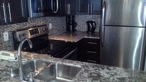 Una cocina moderna con electrodomésticos de acero inoxidable, encimera de granito y muebles negros.