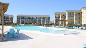 A pool area with lounge chairs and a building with multiple balconies in the background. - Shell Shocked - Oceanfront Surf Condo, Sleeps 6 (Surf City)