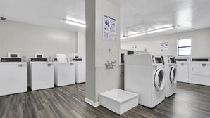 A laundry facility with multiple washing machines and dryers, a white floor, and a sign indicating easy washing. - Shell Shocked - Oceanfront Surf Condo, Sleeps 6 (Surf City)
