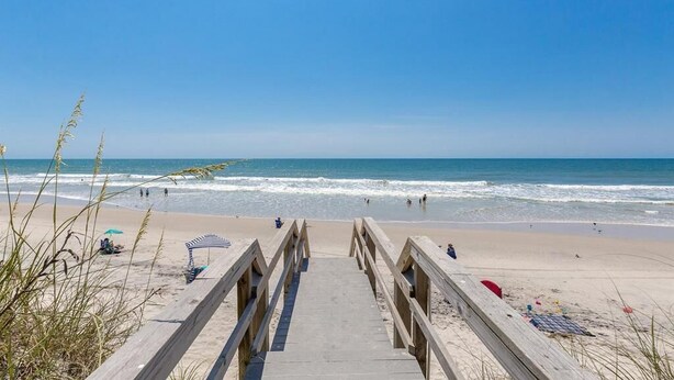 A wooden boardwalk leading to a beach with clear skies and calm waves. - Shell Shocked - Oceanfront Surf Condo, Sleeps 6 (Surf City)