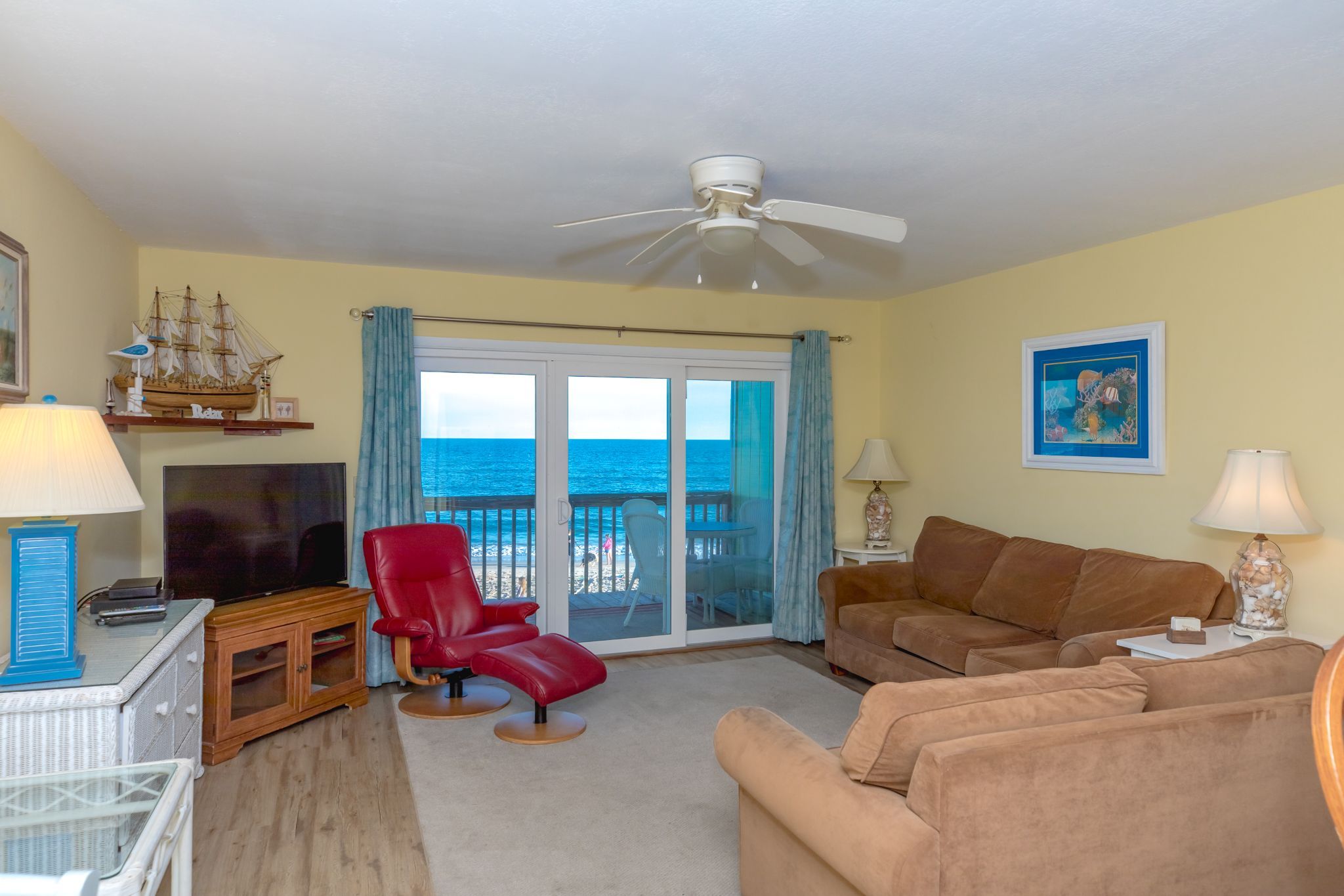 A living room with a television, red and brown sofas, a red chair, and a ceiling fan.