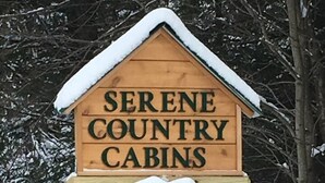 Una señal de madera para Serene Country Cabins con un adorno de coronas nevadas.