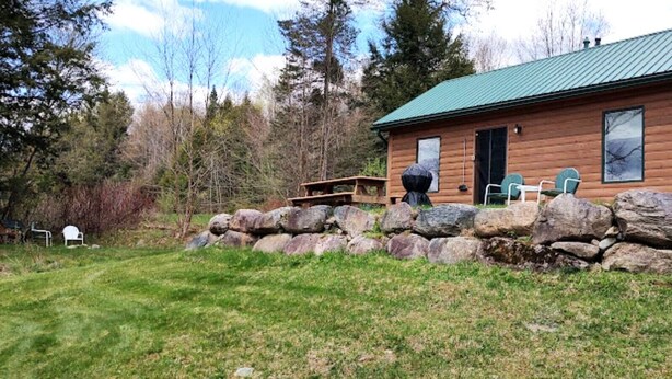 Una cabaña de madera con techo verde, pared de piedra y una mesa de picnic.