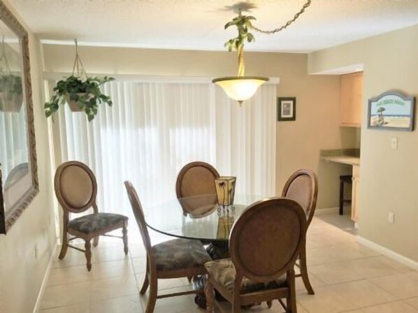 A dining area with a glass table surrounded by four chairs, a hanging plant, and a ceiling light fixture. - Doveplum 810- Very cozy 3BD/2.5BA two story, townhouse overlooking the tranquil canal (Siesta Key)