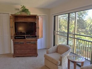A room with a wooden entertainment center, a television, a beige armchair, and a small table.