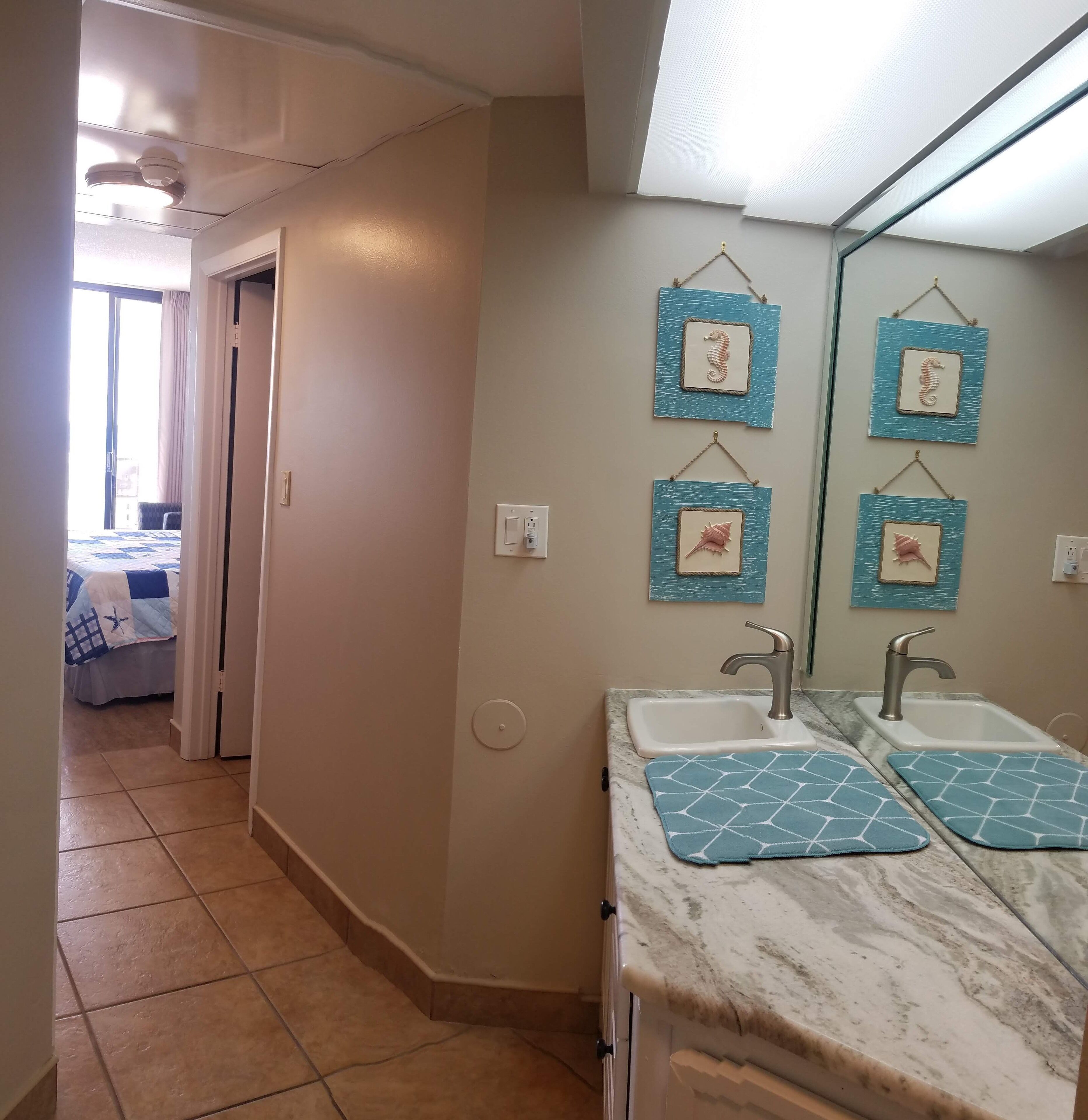A bathroom with two sinks, a mirror, and decorative seahorse wall art.