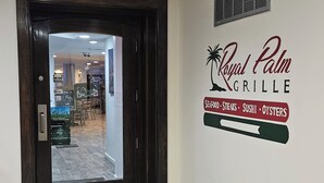 Ein Flur mit einer Tür, die zum Restaurant 'Royal Palm Grille' führt, welches Meeresfrüchte, Steaks, Sushi und Austern serviert.