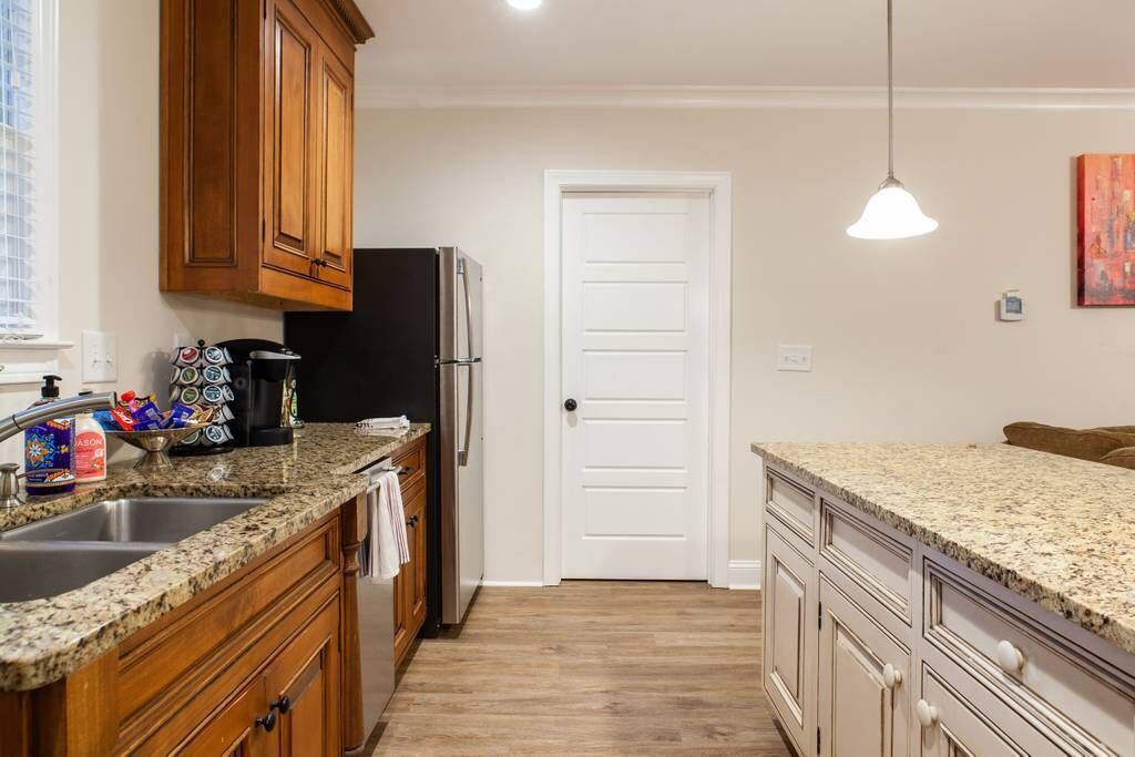 A kitchen with granite countertops, wooden cabinets, a refrigerator, and a white door.