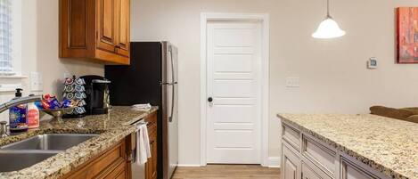 A kitchen with granite countertops, wooden cabinets, a refrigerator, and a white door.