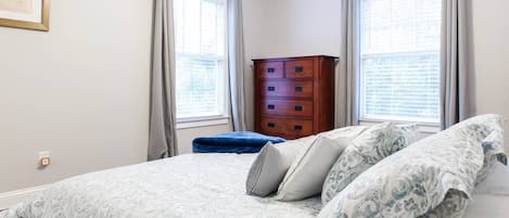 A bedroom with a bed, a dresser, and two windows with curtains.