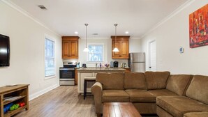 Una cocina moderna con armarios de madera, una isla central, iluminación colgante y un amplio sofá seccional marrón en una sala de estar.