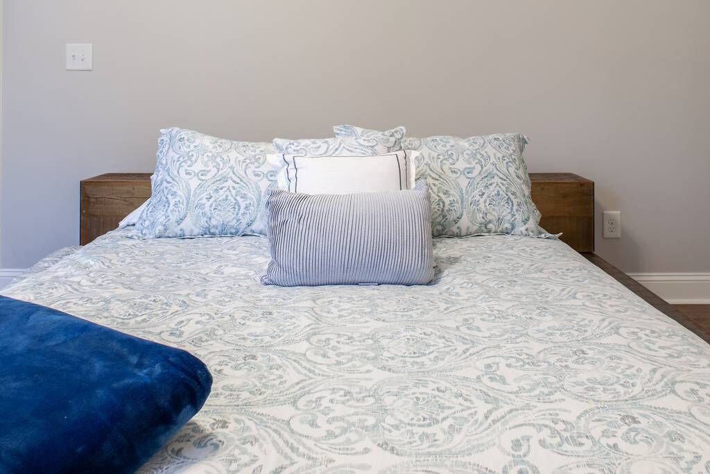 Een bed met beddengoed met een patroon, een blauw kussen en een houten hoofdbord.