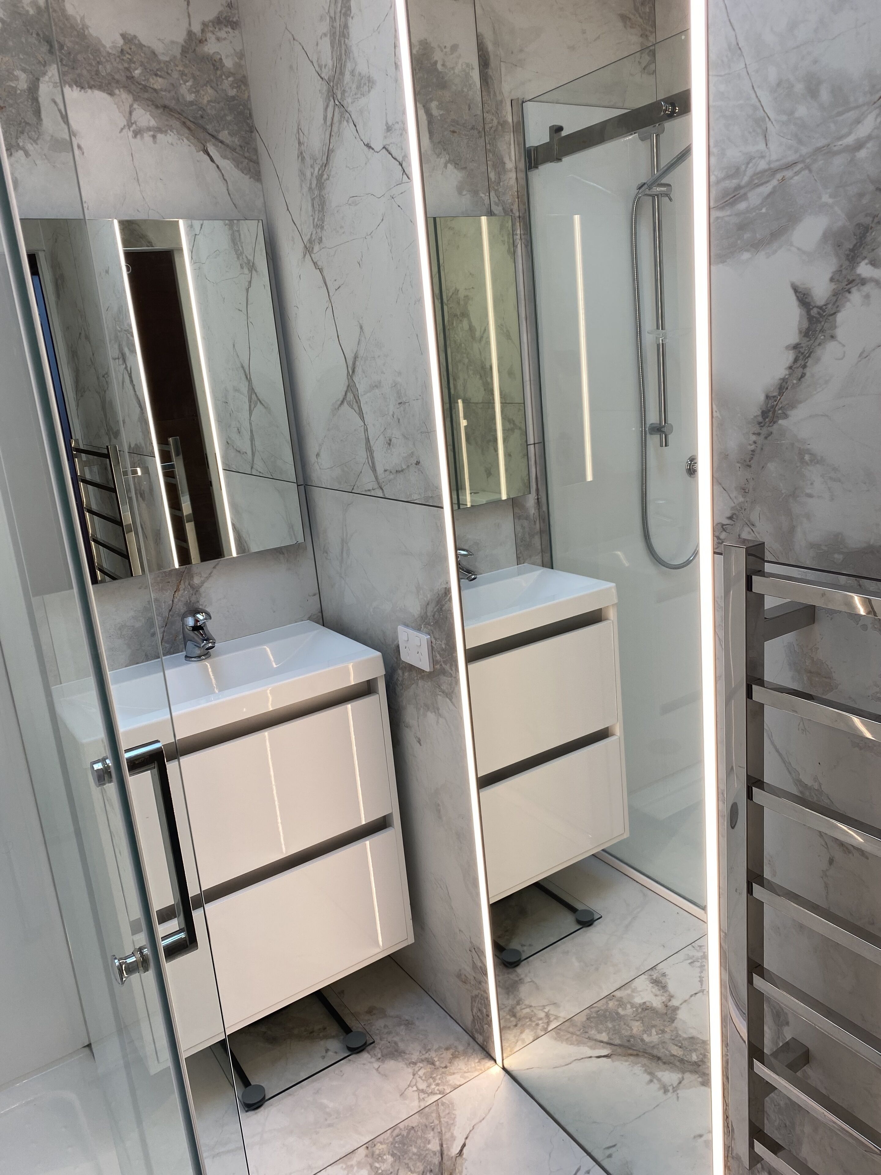 A modern bathroom with a glass-enclosed shower, a white vanity with drawers, and a large mirror.