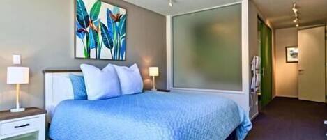 A modern hotel room with a large bed, a nightstand, a wall-mounted painting, and a sliding door leading to another room.