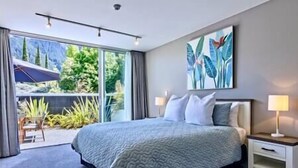 Ein modernes Hotelzimmer mit einem großen Bett, einem Nachttisch, einer Lampe und Blick auf Grün hinter dem Fenster.
