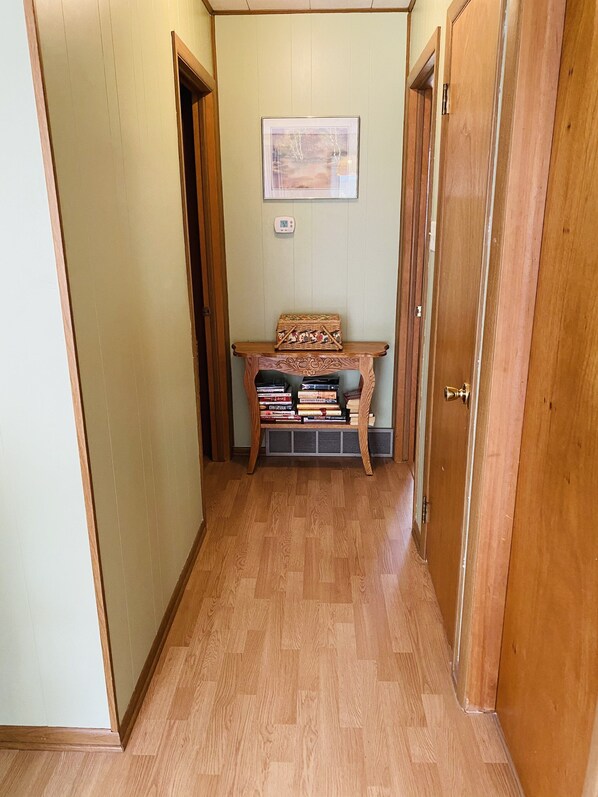 Un pasillo con piso de madera, una pequeña mesa con libros y un cuadro en la pared.
