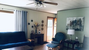 Un salon avec un canapé bleu, une table basse en bois, un fauteuil bleu, une petite table en bois avec une lampe, et un tableau accroché au mur.