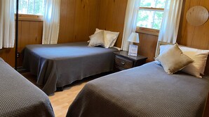 Une chambre avec deux lits, des murs en bois, une table de chevet avec une lampe et une fenêtre avec des rideaux.