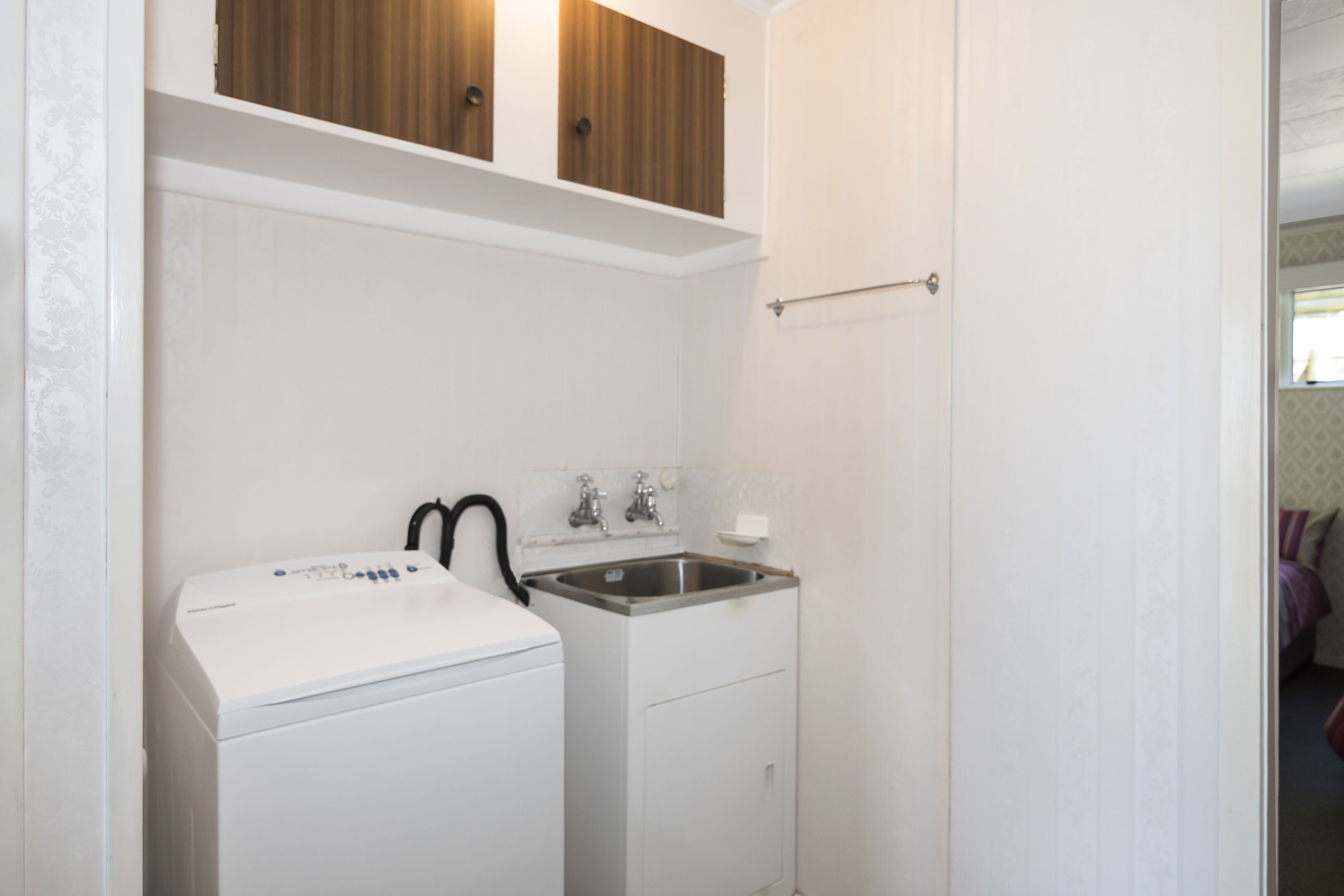 A compact laundry area with a washing machine and a sink, wooden cabinets above, and a towel rack.