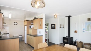 A modern kitchen with wooden cabinets, a dining table, and a wood-burning stove. - Maple's Den - Collingwood beach house (Collingwood)