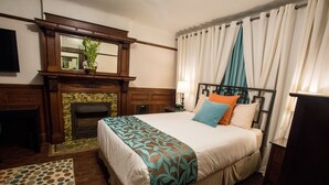 Une chambre d’hôtel avec un lit, une cheminée, un miroir et une fenêtre avec des rideaux.