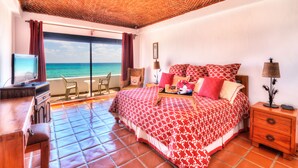 Un dormitorio con una cama, un televisor, un escritorio y una silla. Se ve el océano a través de una ventana.