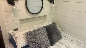 A bed with patterned bedding, two pillows, a decorative grey rug, and wall-mounted light fixtures. - Appalachian Container Cabin (Otto)